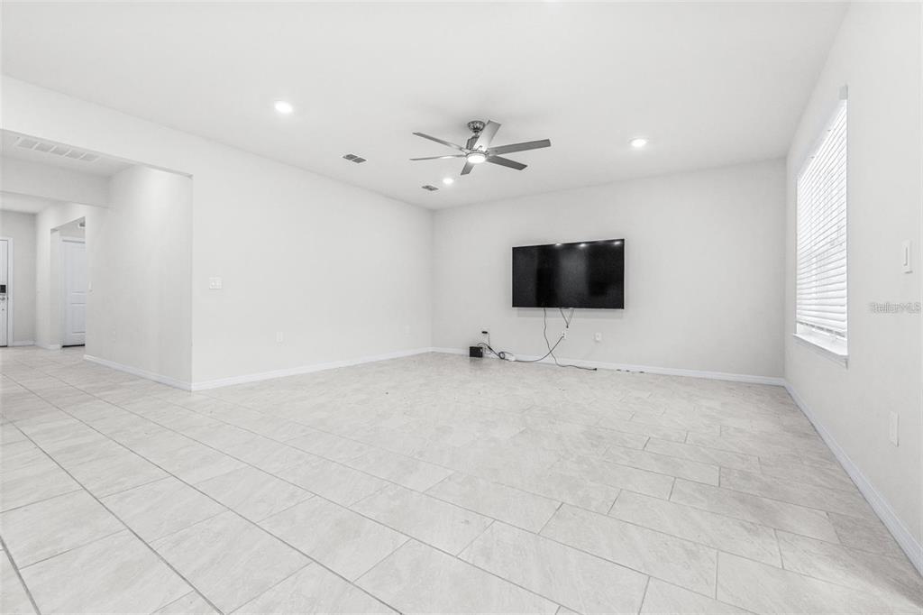A living room features white walls, light tile flooring, a ceiling fan, and a wall-mounted television — 1050 MICHELANGELO LANE, WINTER HAVEN, FL