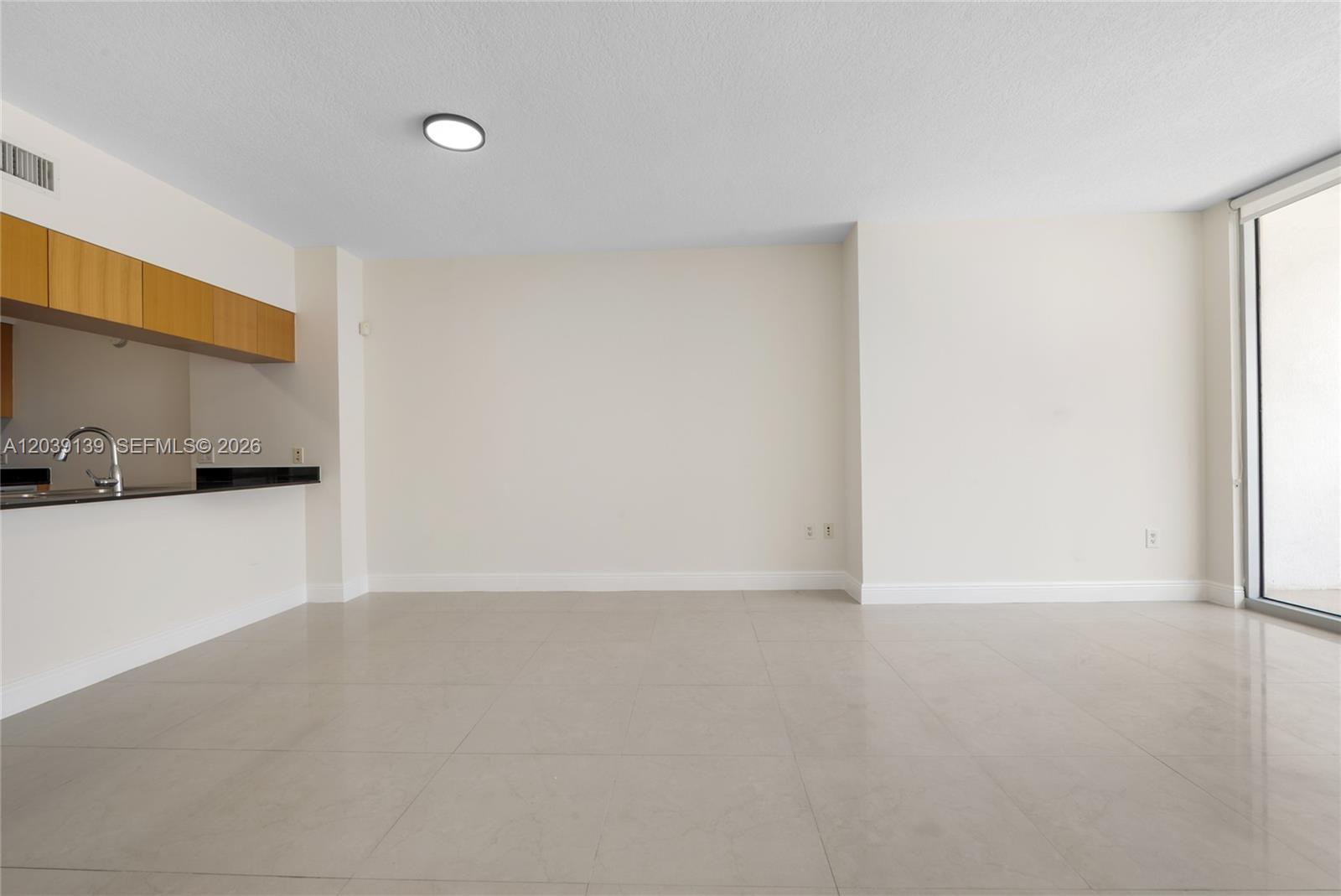An empty room features light-colored tile flooring, a kitchen pass-through, and a sliding glass door — 1750 N Bayshore Dr # 4811, Miami FL 33132, MIAMI, FL