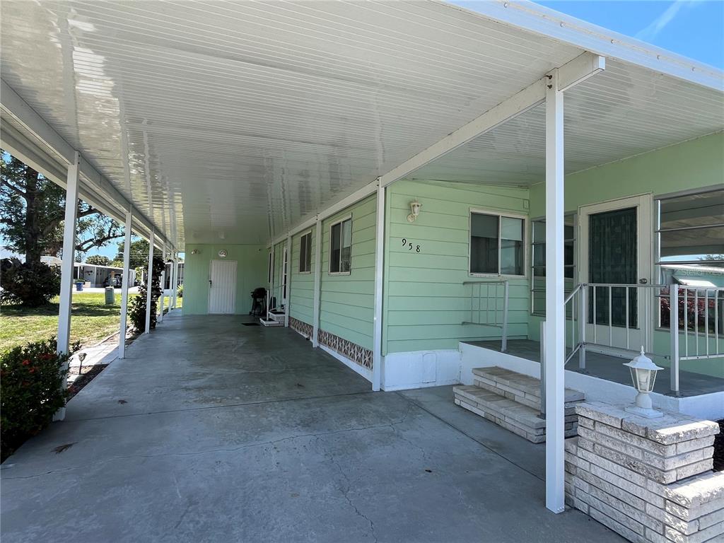 A light green mobile home features a long covered carport and concrete steps leading to the entrance — 958 CORTINA BOULEVARD, VENICE, FL