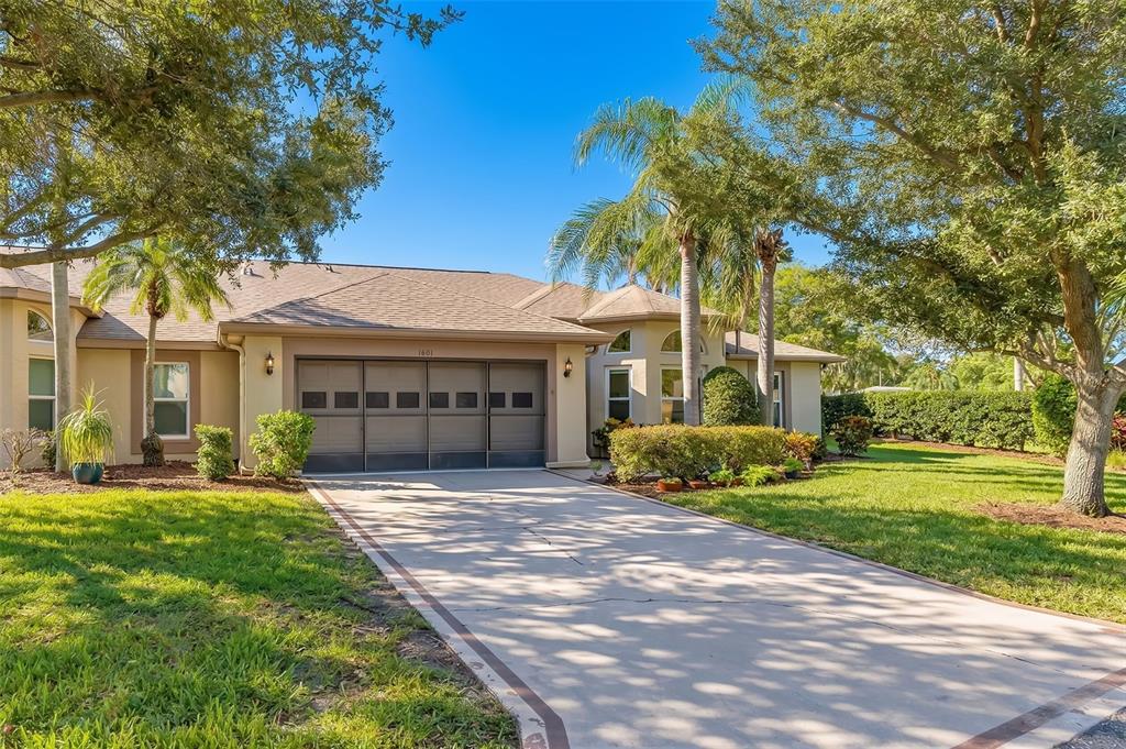 A single-story house with a beige exterior, a multi-car garage, and a concrete driveway — 1601 LAUGHTON PLACE, SUN CITY CENTER, FL