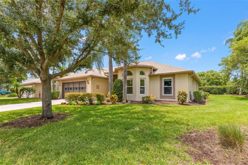 A single-story house with a tan stucco exterior, a two-car garage, and a large tree — 1601 LAUGHTON PLACE, SUN CITY CENTER, FL