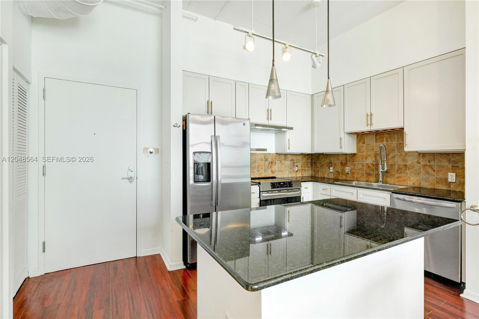 A kitchen features white cabinets, a dark granite island, stainless steel appliances, and tile backsplash — 2001 Biscayne Blvd # 2514, Miami FL 33137, MIAMI, FL