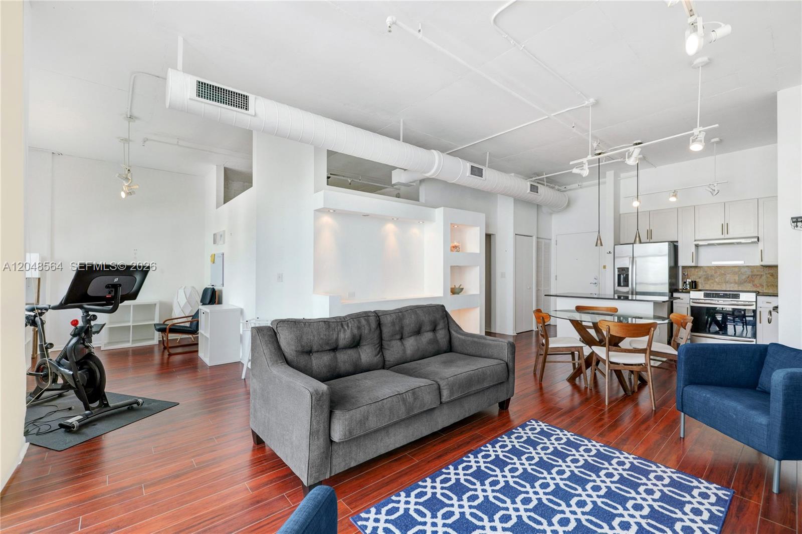 An open-concept living area features a grey sofa, a dining set, and a stationary bike — 2001 Biscayne Blvd # 2514, Miami FL 33137, MIAMI, FL