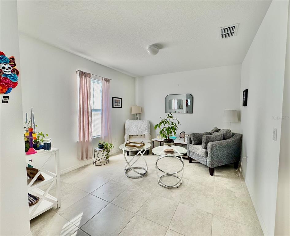 A bright living room features tile flooring, two glass coffee tables, and a gray armchair — 557 PINE TREE BOULEVARD, LAKE ALFRED, FL