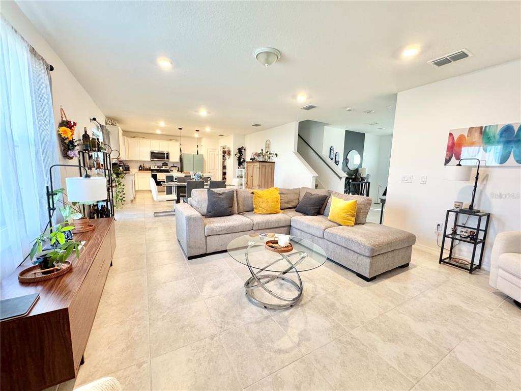 A living room with tile floors, a gray sectional sofa, and an open-concept kitchen — 557 PINE TREE BOULEVARD, LAKE ALFRED, FL