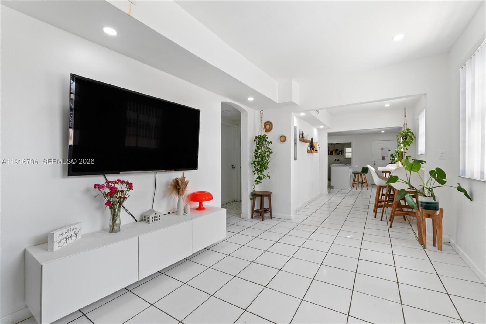 A bright living room features white tile floors, a wall-mounted television, and an open kitchen — 2262 NW 4th St, Miami FL 33125, MIAMI, FL