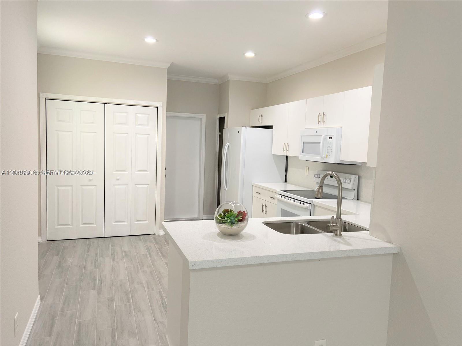 A kitchen features white cabinets, a stainless steel sink, and light-colored wood-look flooring — WESTON, FL