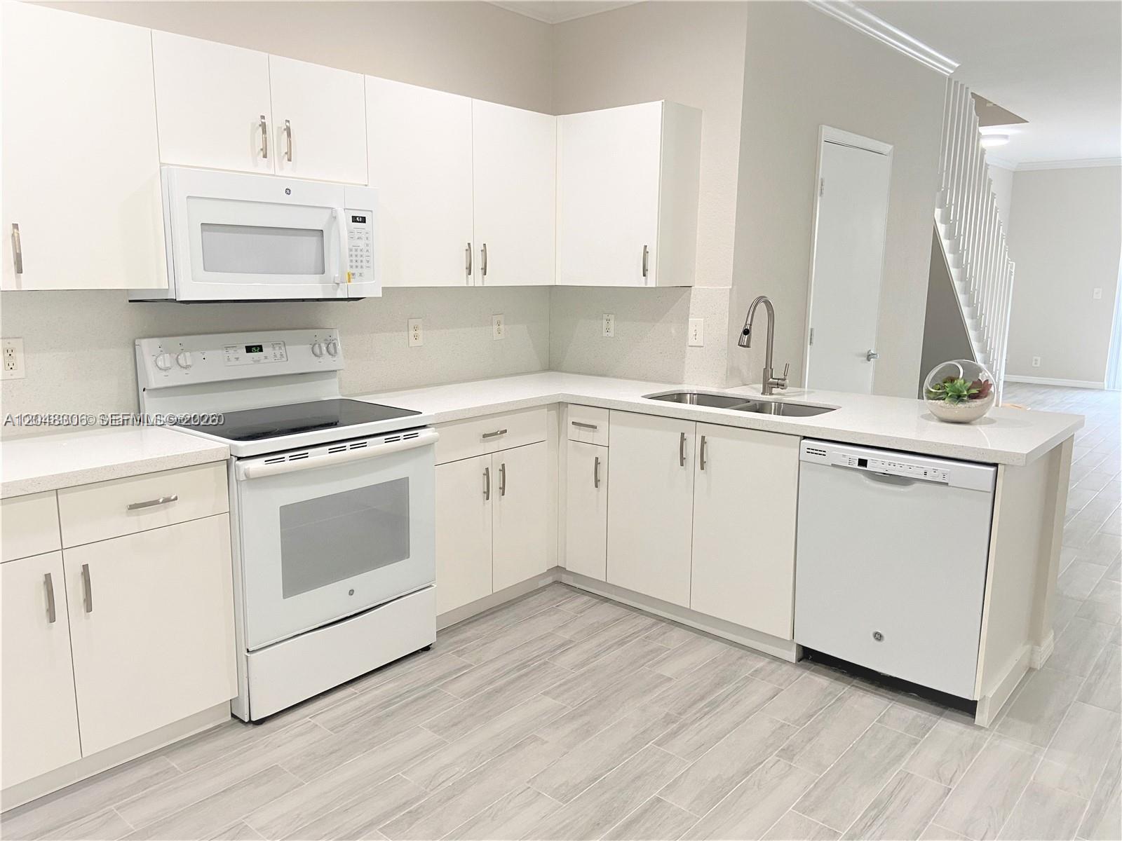 A modern kitchen features white cabinets, white appliances, and light-colored countertops with wood-look tile flooring — WESTON, FL