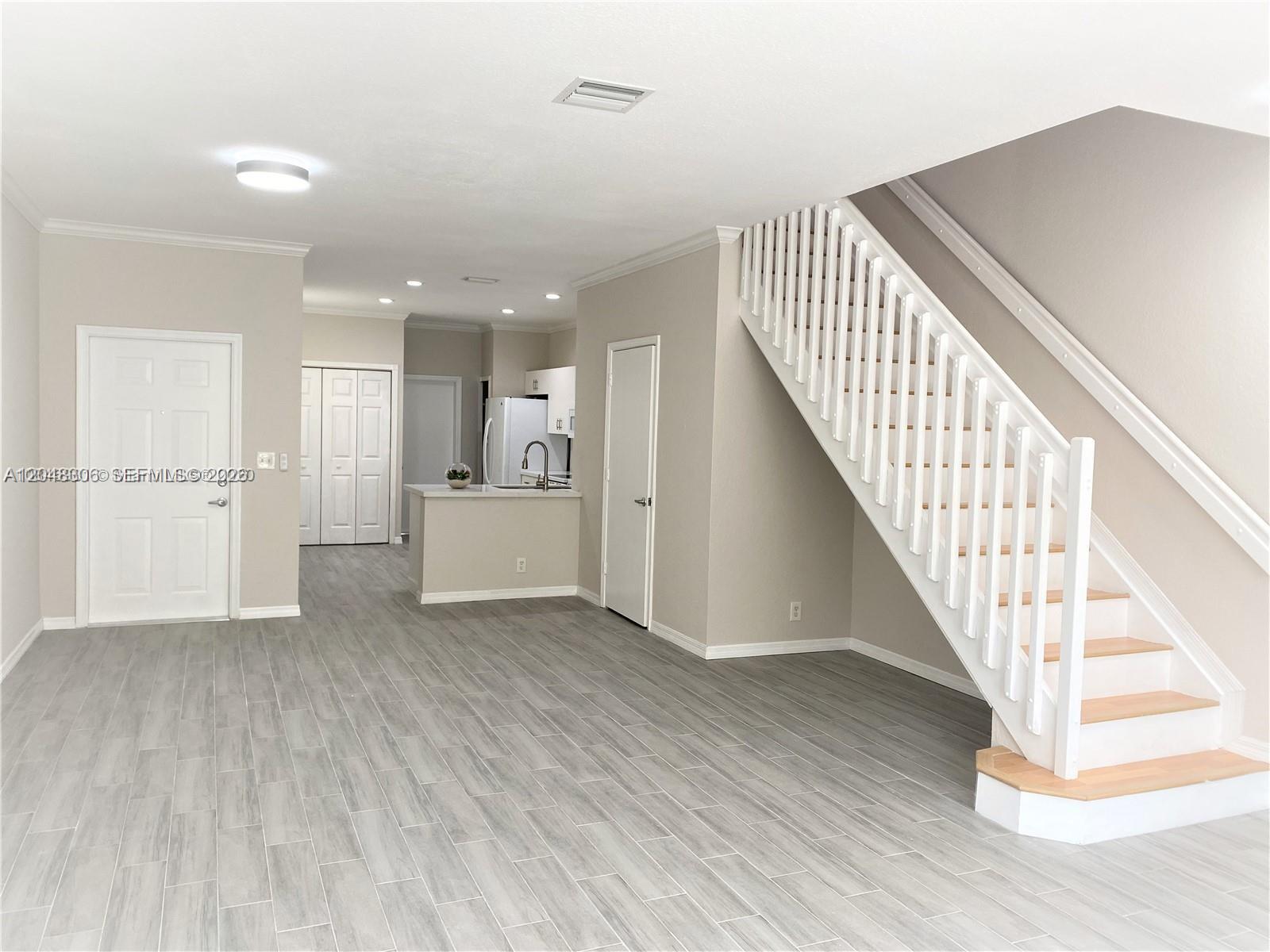 An open-concept living area features light wood-look tile floors, a staircase, and a kitchen — WESTON, FL