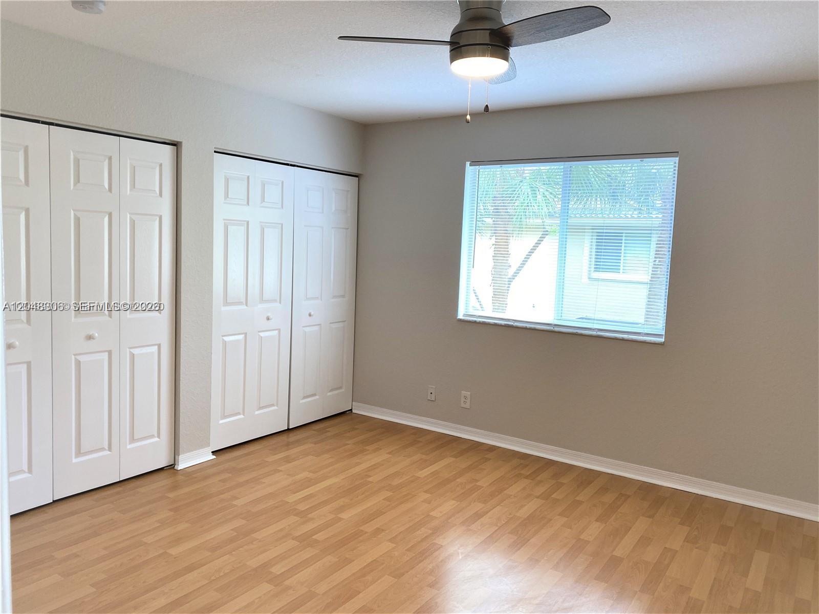 This bedroom features light wood-look flooring, two sets of white closet doors, and a window — WESTON, FL