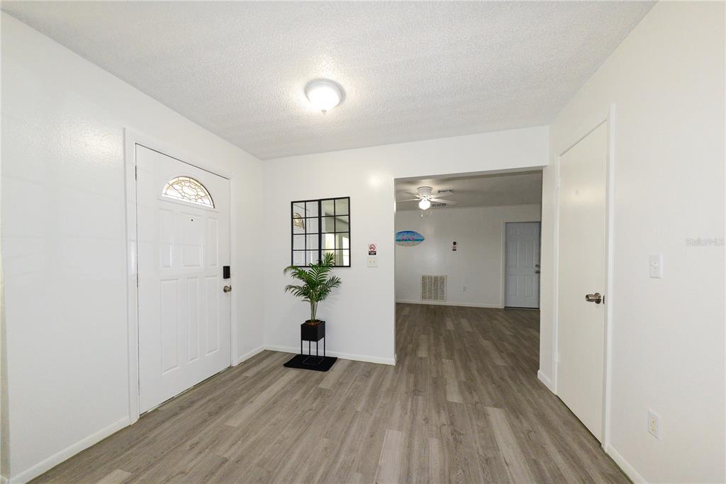 An entryway with light wood-look flooring, white walls, a front door, and a small plant — 124 CADDY ROAD, ROTONDA WEST, FL