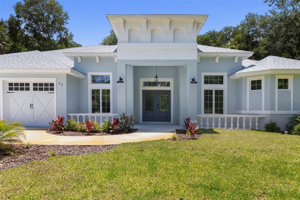 A light blue single-story house with a central tower, double front doors, and a garage — 73 BRIDLE RIDGE COURT, FLAGLER BEACH, FL