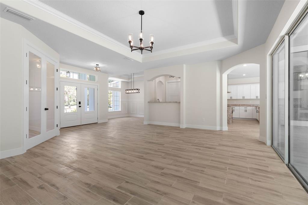 An open-concept living area features light wood-look tile flooring, a tray ceiling, and white walls — 73 BRIDLE RIDGE COURT, FLAGLER BEACH, FL