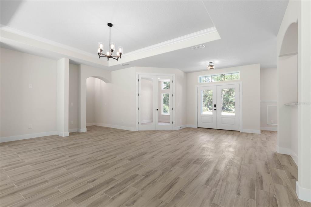 A bright, empty room features light wood-look tile flooring, a tray ceiling, and French doors — 73 BRIDLE RIDGE COURT, FLAGLER BEACH, FL