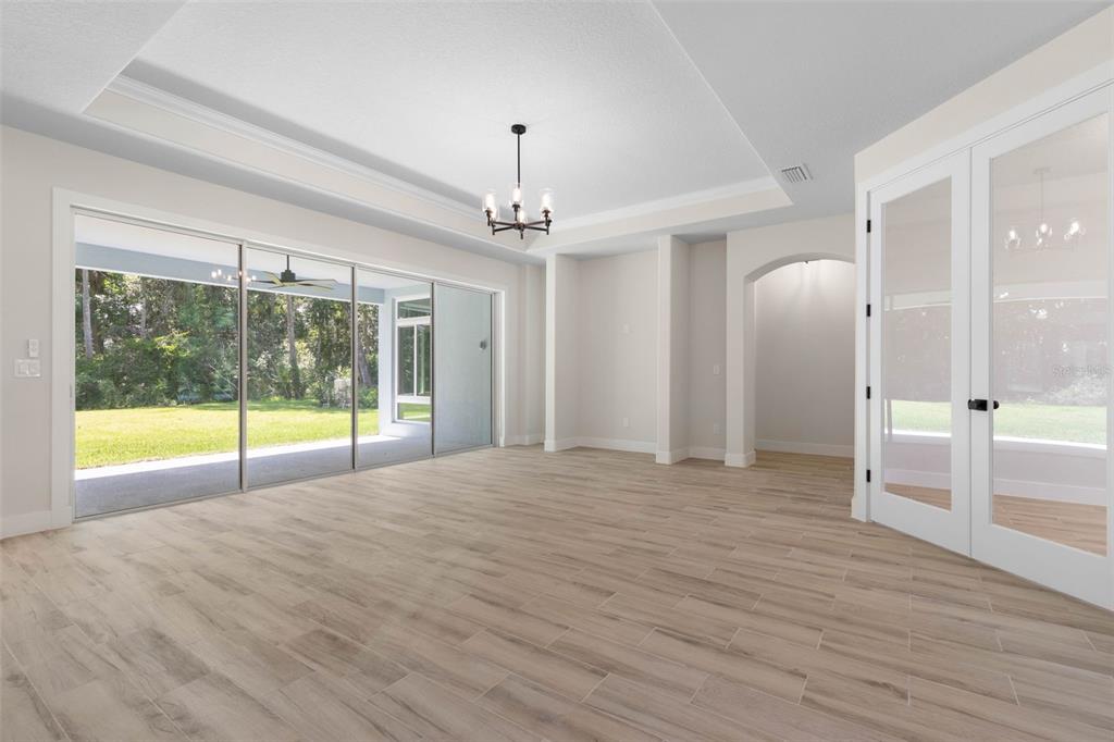 A bright living room features wood-look tile floors, a tray ceiling, and large sliding glass doors — 73 BRIDLE RIDGE COURT, FLAGLER BEACH, FL