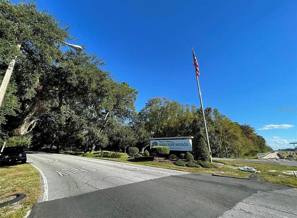 A road leads to a sign for Sugarmill Woods under a clear blue sky — 16 MAYTEN COURT N, HOMOSASSA, FL