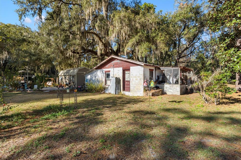 A small, single-story block house with a red roof sits on a grassy, tree-filled lot — 1582 S US 301, SUMTERVILLE, FL