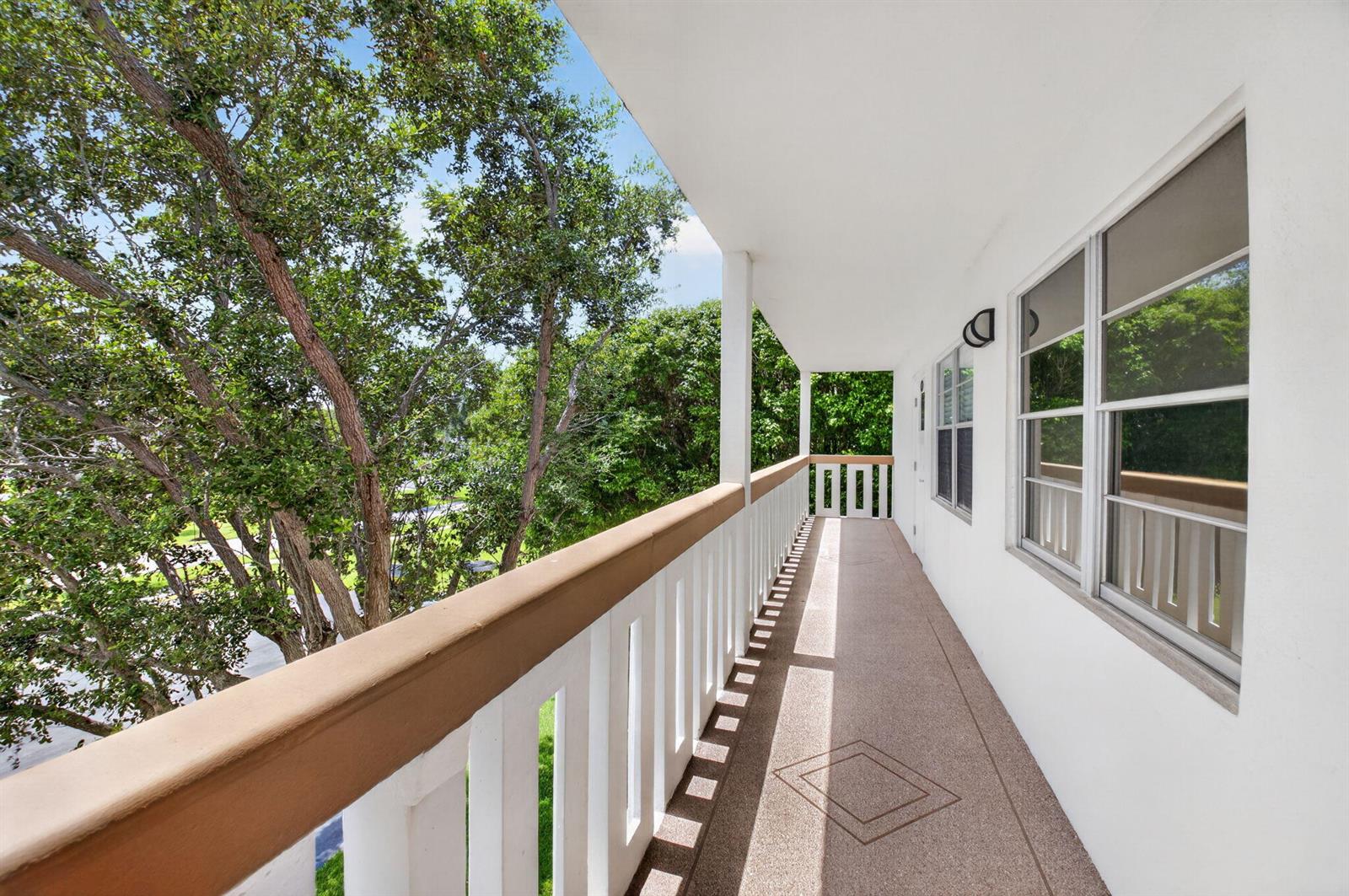 A covered outdoor balcony features white railings, a textured floor, and views of nearby trees — 3080 Cornwall D, Boca Raton FL 33434, BOCA RATON, FL