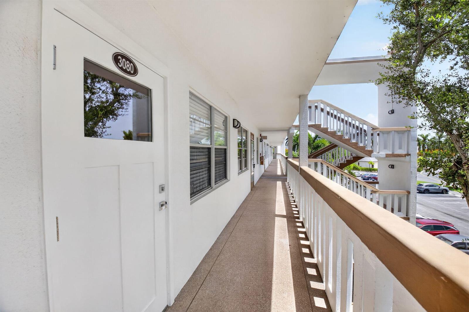 An exterior walkway leads past apartment doors toward a staircase in a multi-story building — 3080 Cornwall D, Boca Raton FL 33434, BOCA RATON, FL