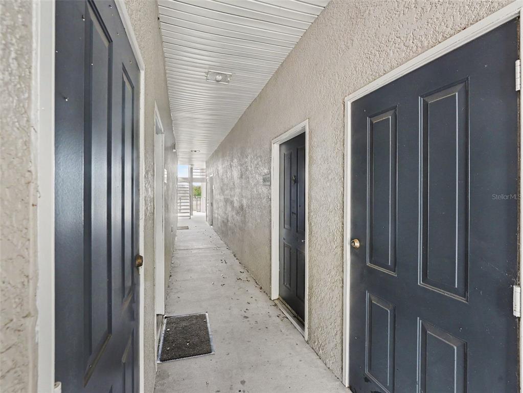 A narrow outdoor apartment hallway features concrete flooring and several dark blue entry doors — 8003 HEMINGWAY CIRCLE UNIT 8003-8, HAINES CITY, FL