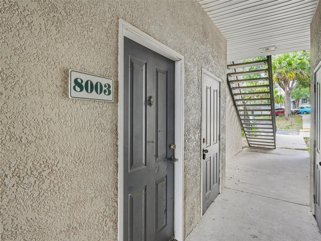 A view of an apartment entrance with a numbered sign and an adjacent metal staircase — 8003 HEMINGWAY CIRCLE UNIT 8003-8, HAINES CITY, FL