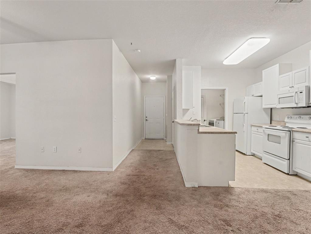 A view of a carpeted living area leading to a kitchen with white appliances — 8003 HEMINGWAY CIRCLE UNIT 8003-8, HAINES CITY, FL