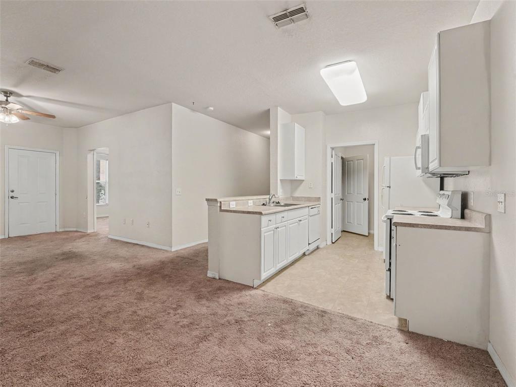 An open-concept kitchen with white cabinets and a breakfast bar overlooks a carpeted living area — 8003 HEMINGWAY CIRCLE UNIT 8003-8, HAINES CITY, FL