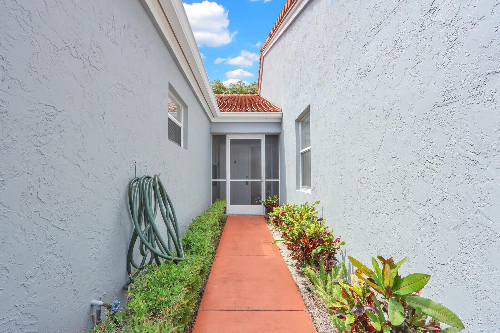 A concrete walkway leads to a screened front door between two light-colored stucco walls — 9904 Summerbrook Terrace # B, Boynton Beach FL 33437, BOYNTON BEACH, FL