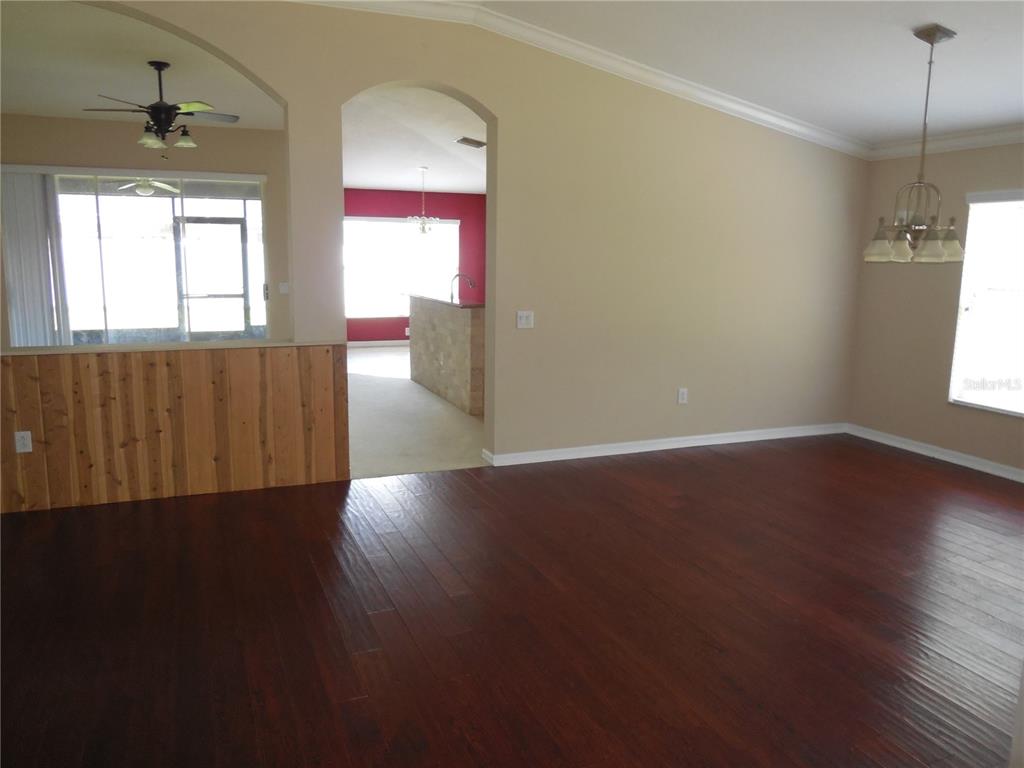 A living room with dark wood flooring, beige walls, and an arched entryway to a kitchen — 15447 OSPREY GLEN DRIVE, LITHIA, FL