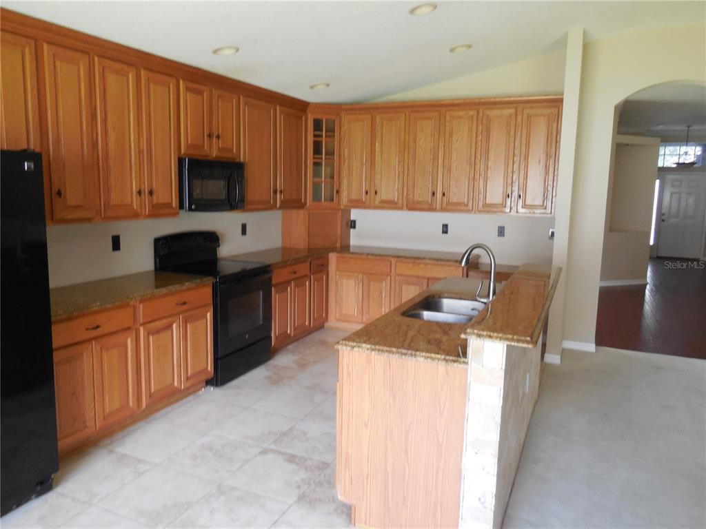 A kitchen with oak cabinets, granite countertops, a black stove, and a central island — 15447 OSPREY GLEN DRIVE, LITHIA, FL