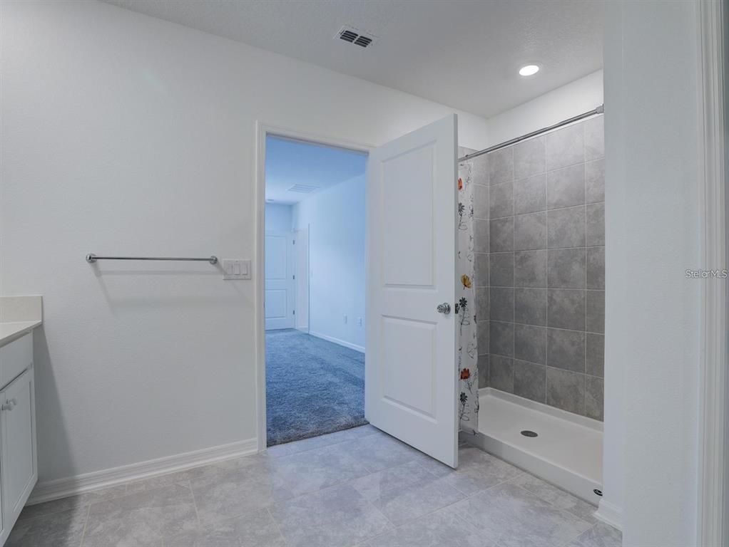A bathroom features a tiled shower, a white vanity, and a doorway leading to a bedroom — 602 BELL PRAIRIE CIRCLE, LAKE WALES, FL