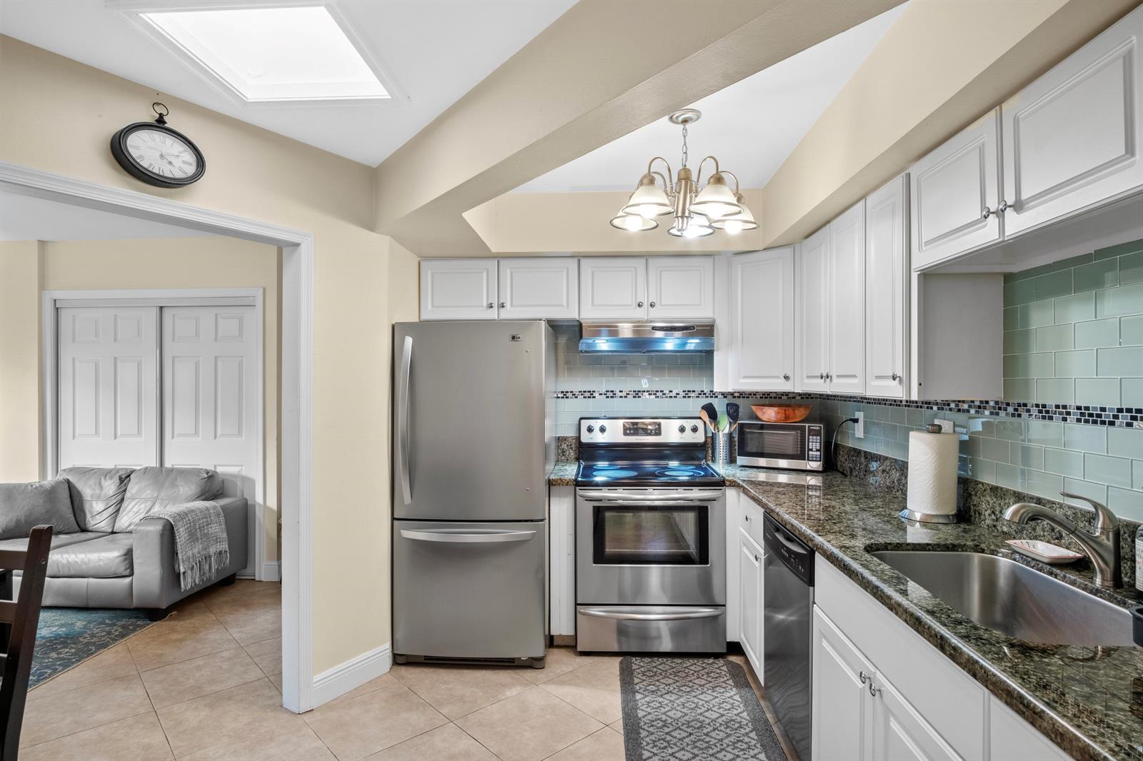A kitchen with white cabinets, stainless steel appliances, and granite countertops opens to a living area — 803 NE 2nd Avenue, Delray Beach FL 33444, DELRAY BEACH, FL