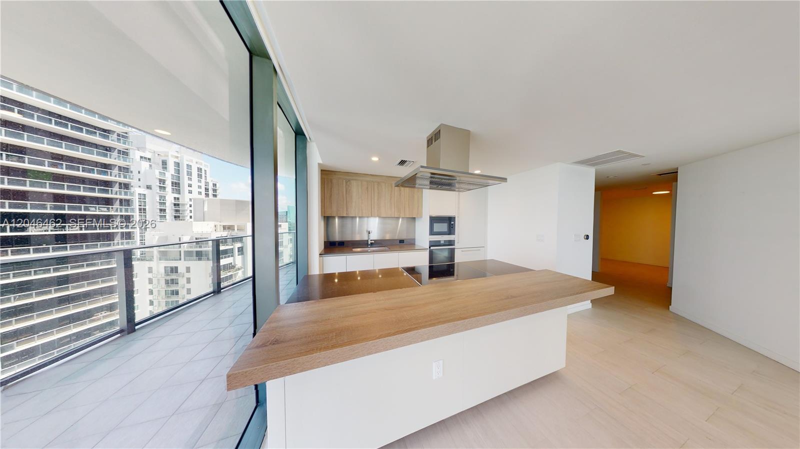 A modern kitchen features a wooden breakfast bar, white cabinetry, and a balcony with city views — 1000 Brickell Plaza # 3915, Miami FL 33131, MIAMI, FL