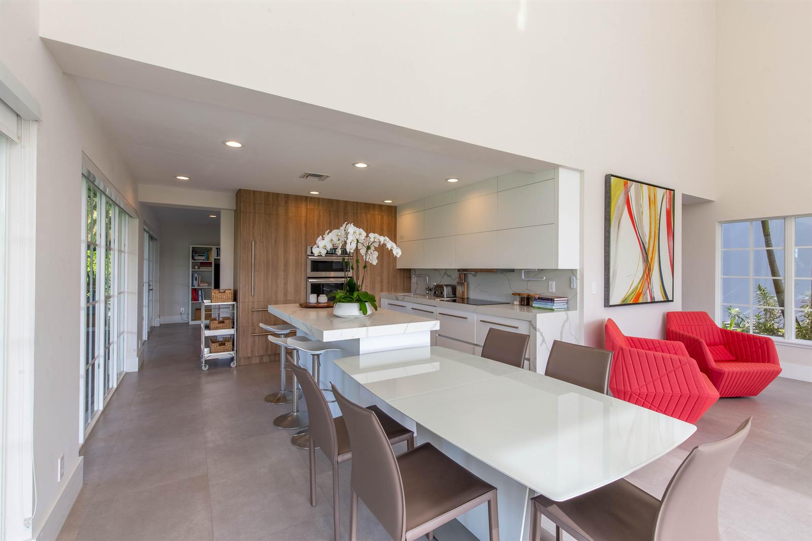 A modern kitchen features a white island, wood cabinetry, and a dining table with chairs — 14432 Rolling Rock  (house) Place, Wellington FL 33414, WELLINGTON, FL