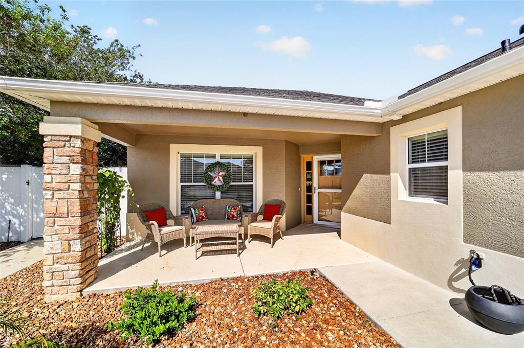 A covered patio features wicker furniture, a stone pillar, and a gravel garden bed — 628 BERMUDEZ COURT, THE VILLAGES, FL
