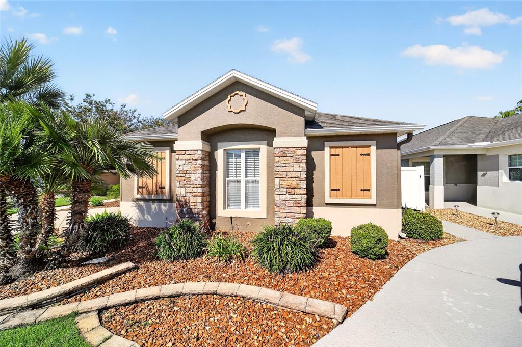 A single-story house exterior features a stone-accented facade, tan stucco, and a curved driveway — 628 BERMUDEZ COURT, THE VILLAGES, FL