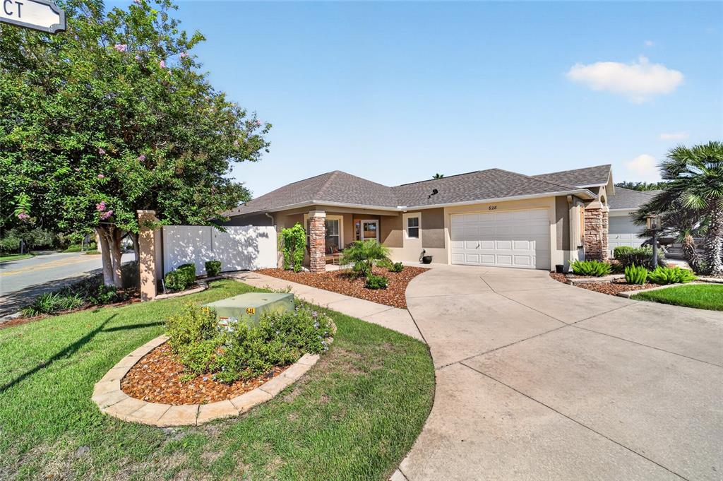 A single-story house with a beige exterior, stone accents, and a concrete driveway — 628 BERMUDEZ COURT, THE VILLAGES, FL