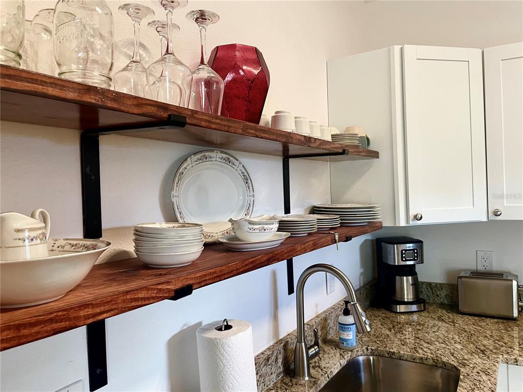 A kitchen features open wooden shelving with dishware above a granite countertop and sink — 1484 CLEVELAND STREET, CLEARWATER, FL