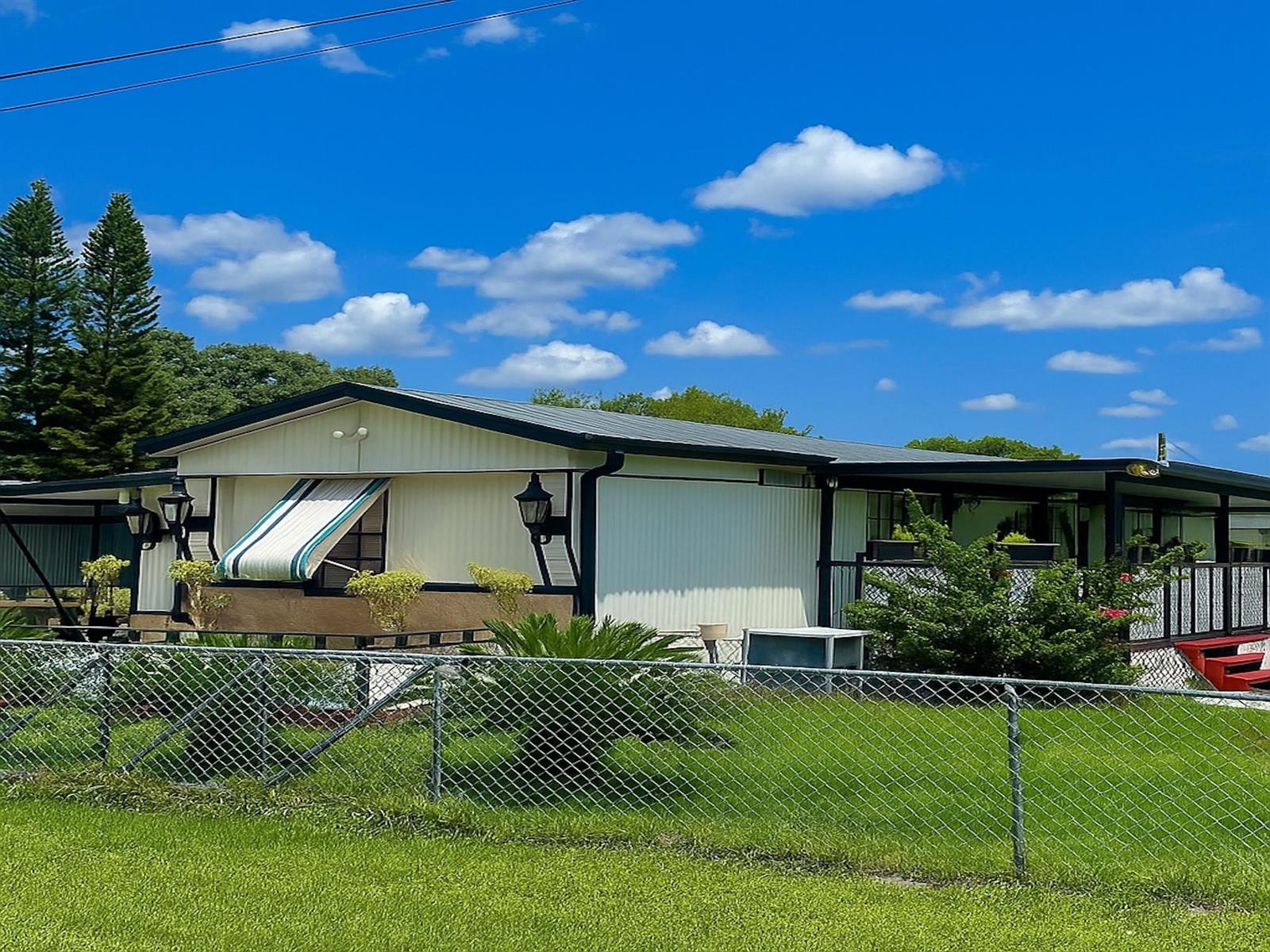 A single-story mobile home with a metal roof, striped awning, and chain-link fence — 4143 SE 29th Court, Okeechobee FL 34974, OKEECHOBEE, FL
