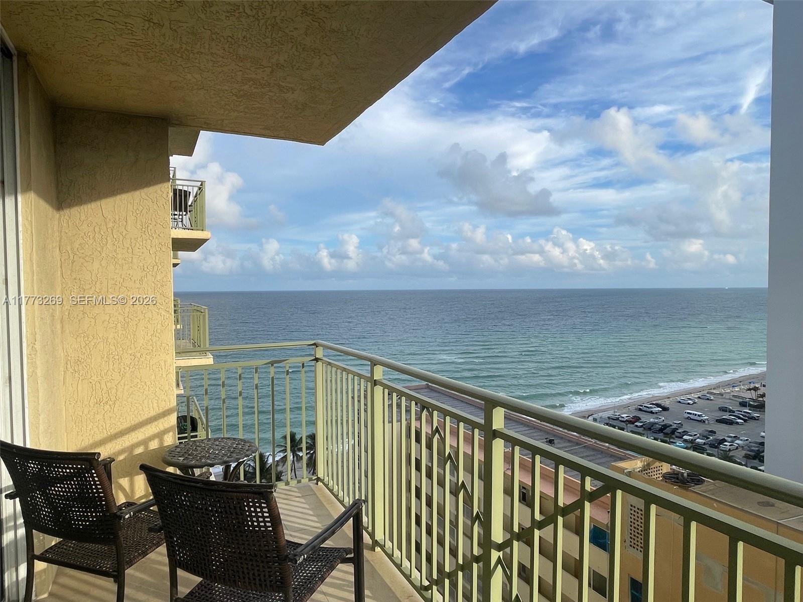 A balcony with two chairs and a small table overlooks the ocean and parking lot — 2080 S Ocean Dr # 1405, Hallandale Beach FL 33009, HALLANDALE BEACH, FL