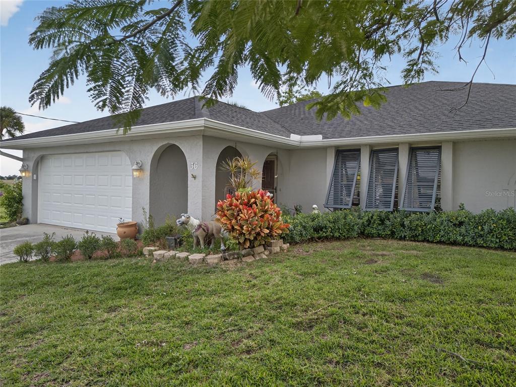 A single-story house with a white garage, arched entryway, and gray shutters on the windows — 36 BUNKER LANE, ROTONDA WEST, FL