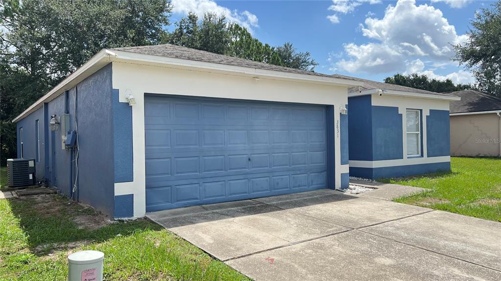 A blue house with a two-car garage and a concrete driveway under a blue sky — 3831 CINNAMON FERN LOOP, CLERMONT, FL