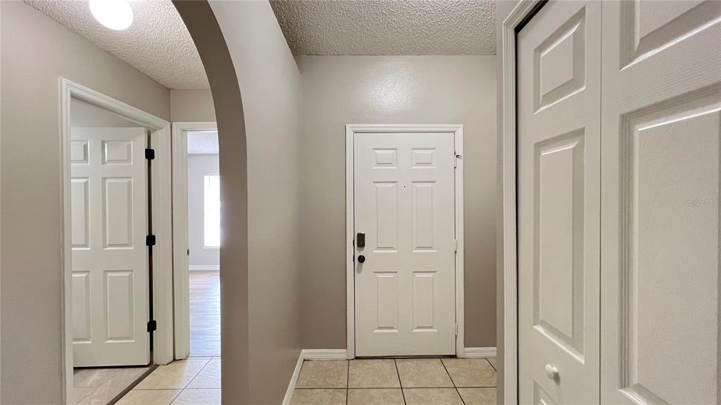An entryway features a white front door, tiled floor, arched doorway, and a closet — 3831 CINNAMON FERN LOOP, CLERMONT, FL
