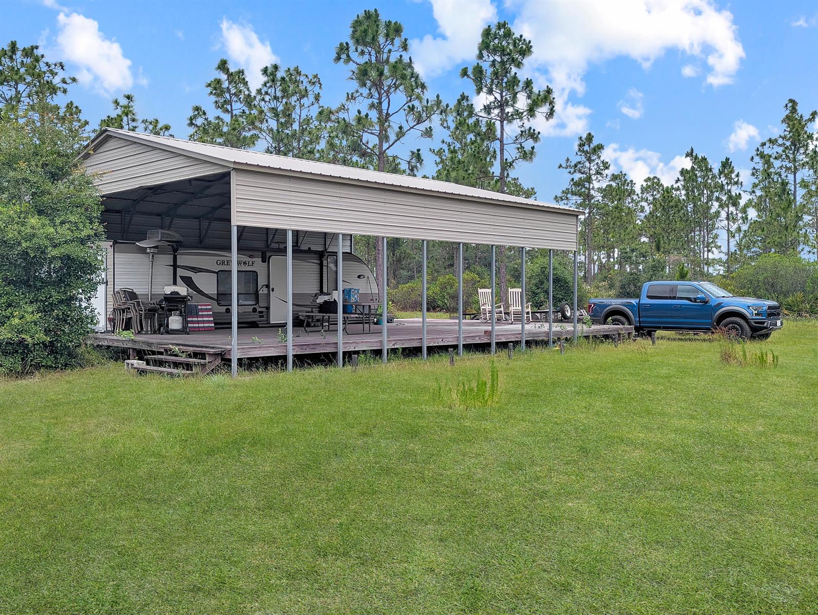 A travel trailer is parked under a large metal carport structure on a wooden deck — 0 Holopaw Groves Road, FL 34771, FL