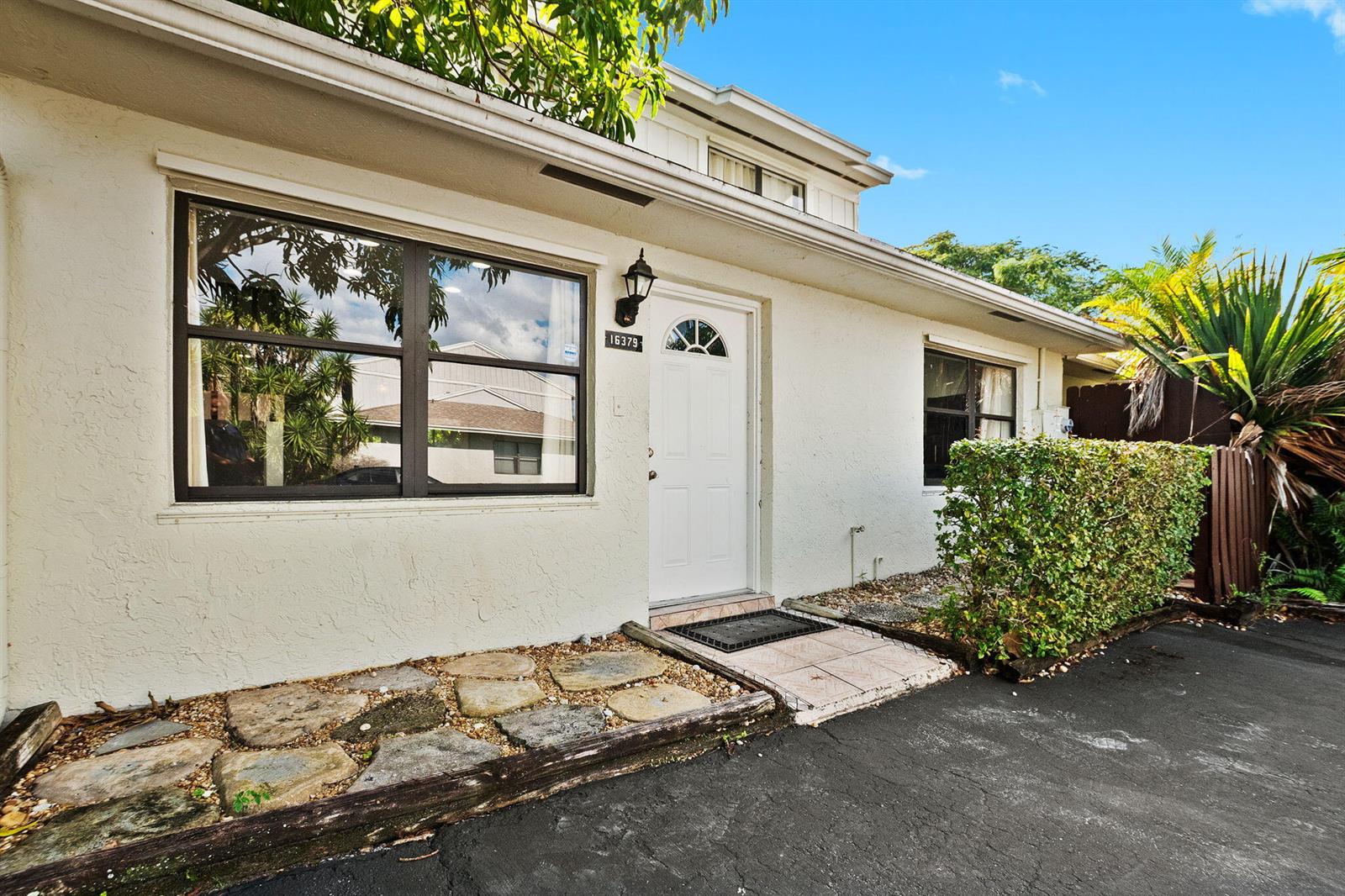The exterior of a single-story home features a white door, large windows, and stone landscaping — 16379 Water Way, Delray Beach FL 33484, DELRAY BEACH, FL