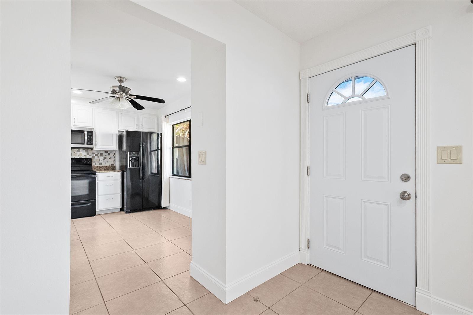 A white front door opens into a tiled entryway leading to a kitchen with black appliances — 16379 Water Way, Delray Beach FL 33484, DELRAY BEACH, FL
