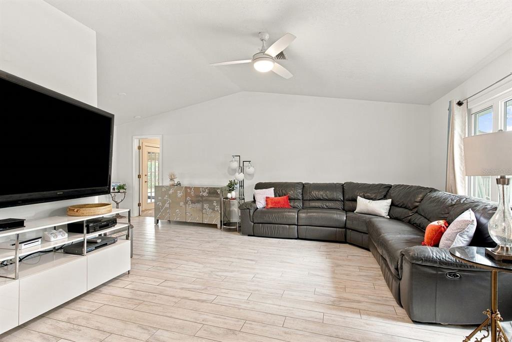 A living room features a large sectional sofa, a television, and light wood-look tile flooring — 1111 CARLTON ROAD, TARPON SPRINGS, FL