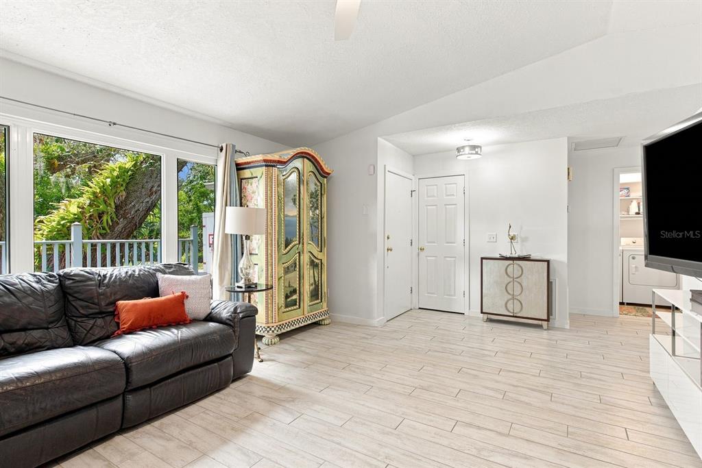 A living room features light wood-look tile floors, a dark leather sofa, and a painted armoire — 1111 CARLTON ROAD, TARPON SPRINGS, FL