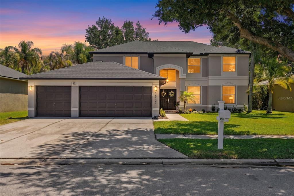 A two-story house with a three-car garage and a concrete driveway at sunset — 16127 LYTHAM DRIVE, ODESSA, FL