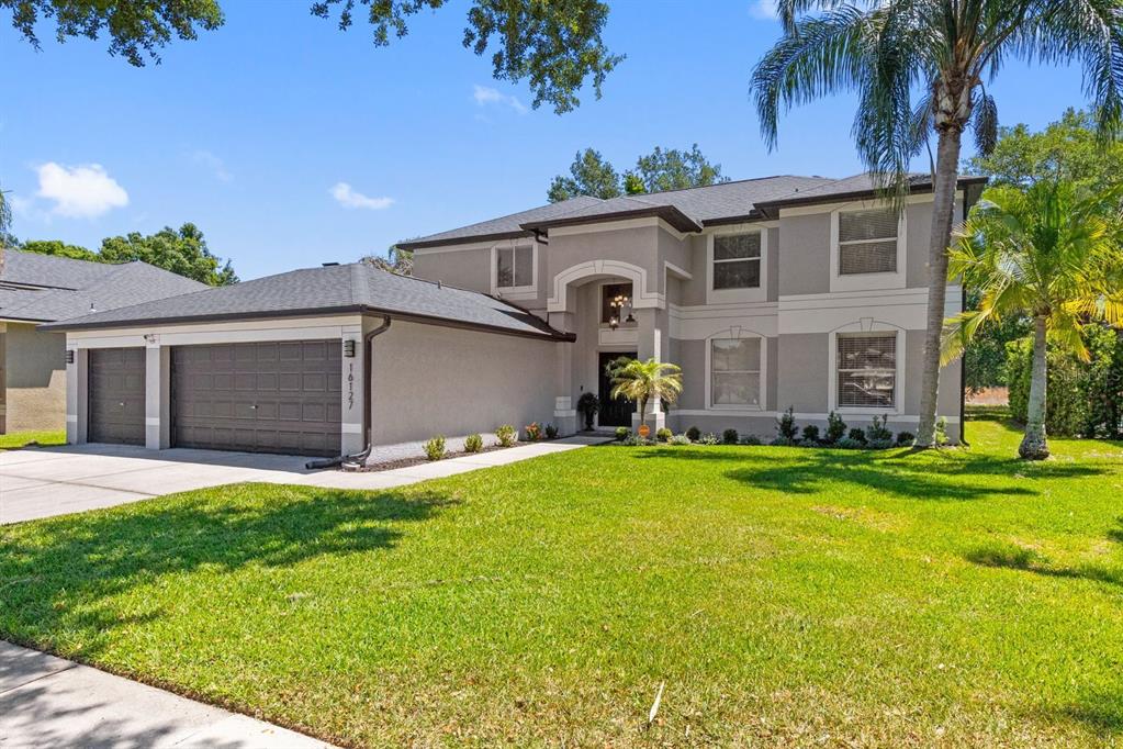 A two-story house with a gray stucco exterior, a three-car garage, and a front lawn — 16127 LYTHAM DRIVE, ODESSA, FL